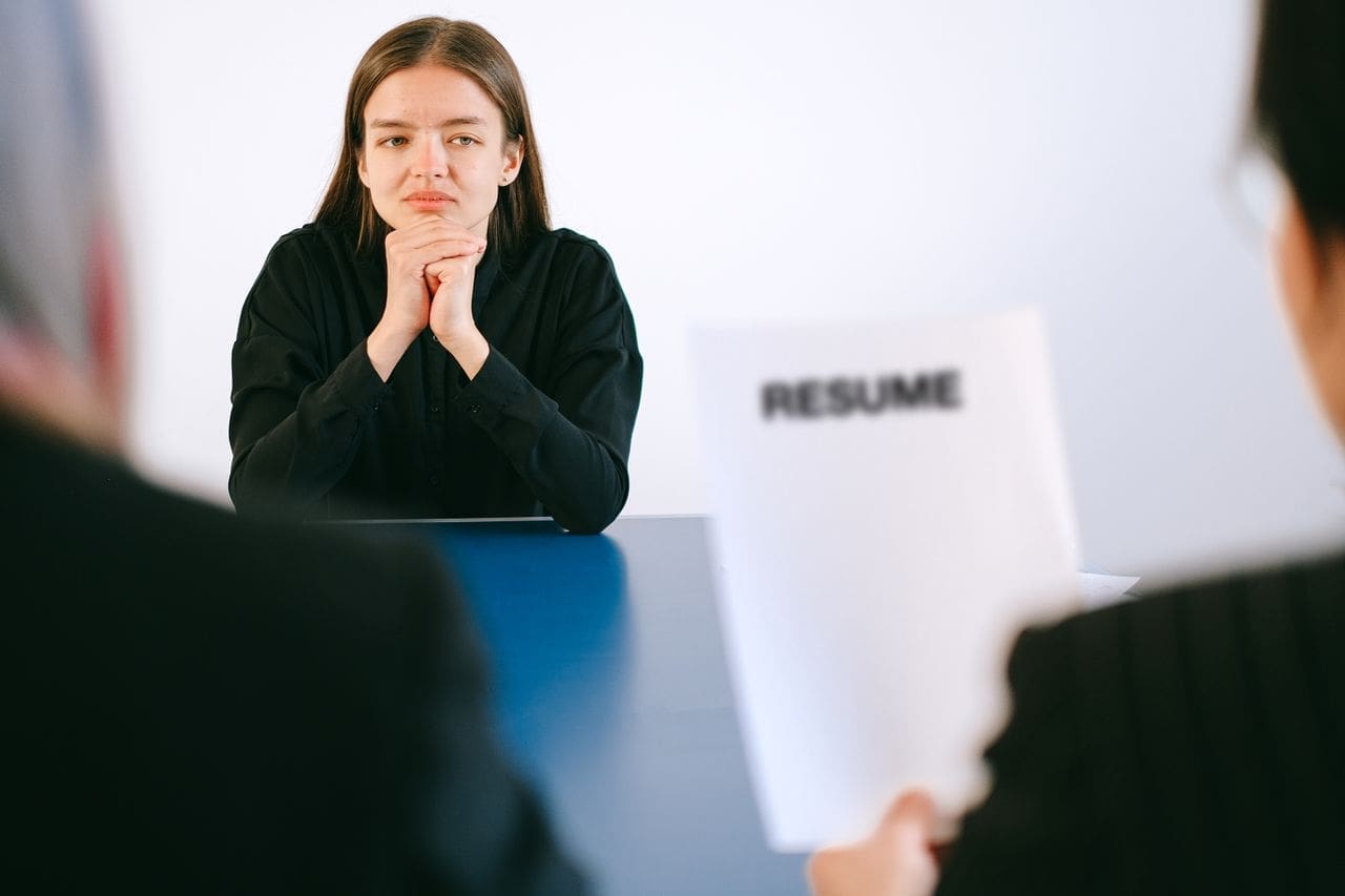 services-01 A woman in a job interview facing two employers with a focus on her resume.